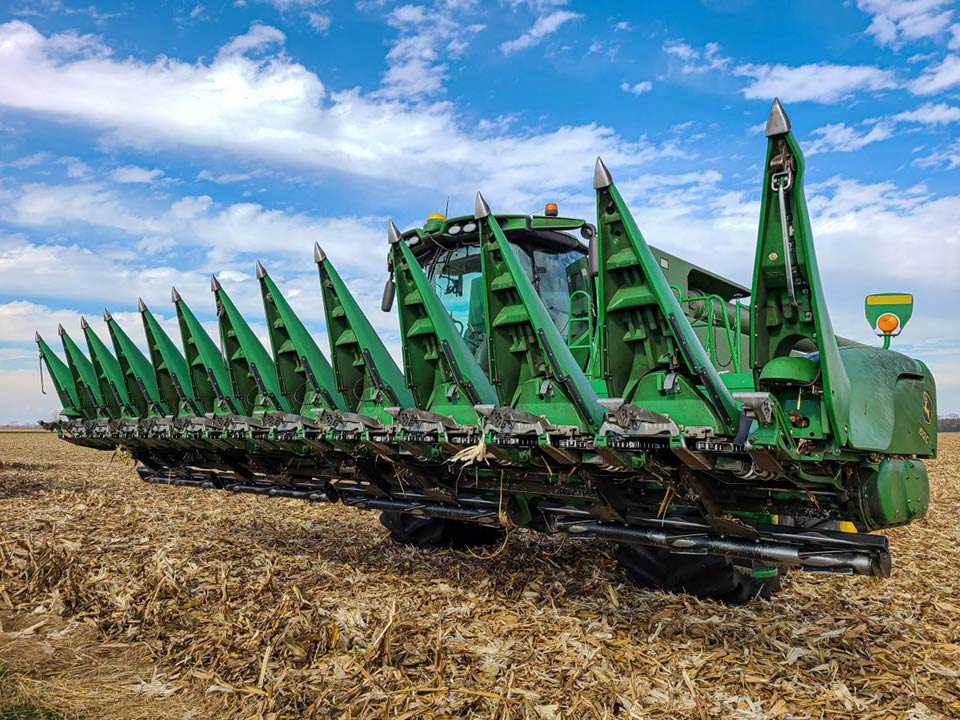 front view of a combine parked in crushed cornstalks, with snouts on corn head raised to show Stalk Devastators